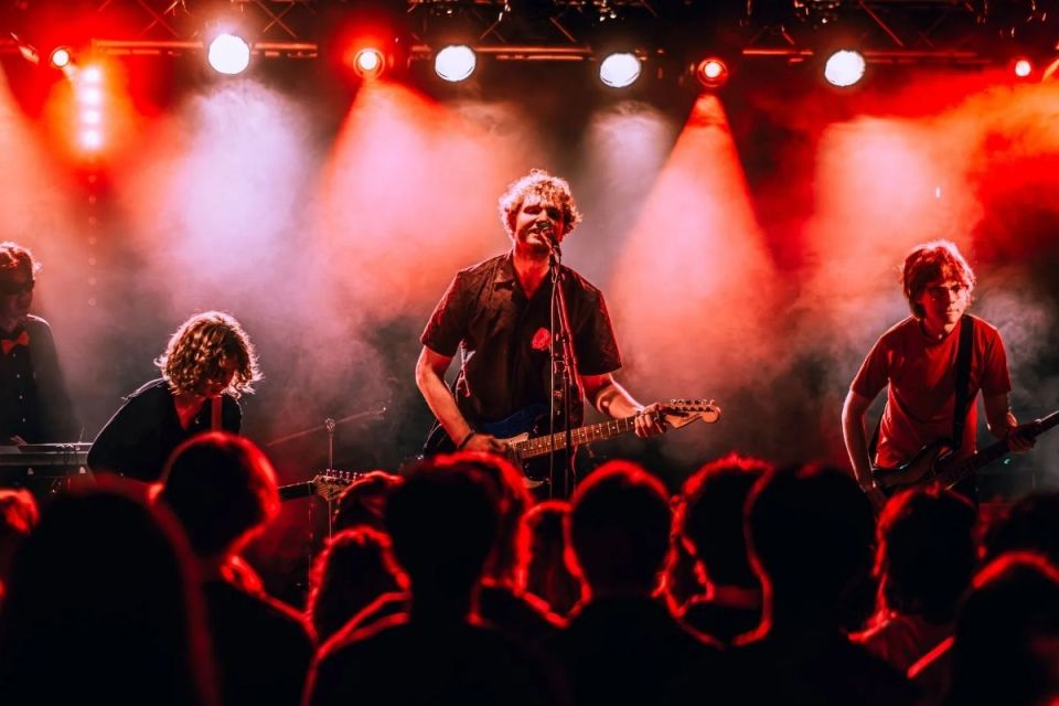 Ett band på scen med rött ljus bakom, och en publik framför.