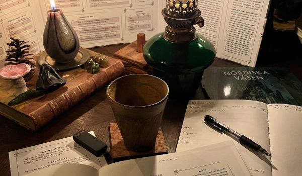 Rollspelsböcker, tärningar och anteckningsblock på ett bord upplyst av levande ljus och en fotogenlampa.