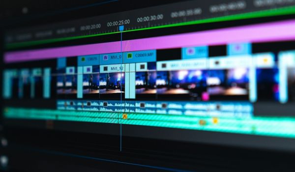 Närbild på en digital tidslinje under filmredigering med färgstarka videoklipp och ljudvågor i fokus.