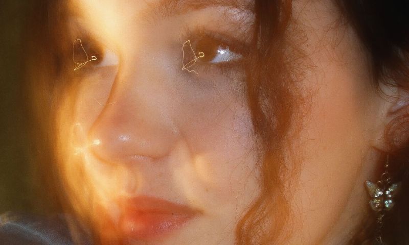 Närbild i varmt ljus på krönikören Lovisa Fhager. Hon har lockigt hår och ett glittrigt fjärilsörhänge.