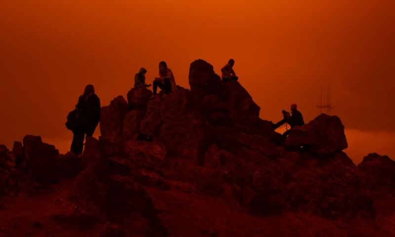 Silhuetter av personer som sitter på klippor mot en starkt orange, dimmig himmel.