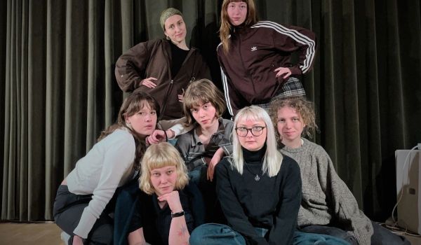 Nära gruppbild på sju unga vuxna i olika stilar, mot mörk drakplagg.