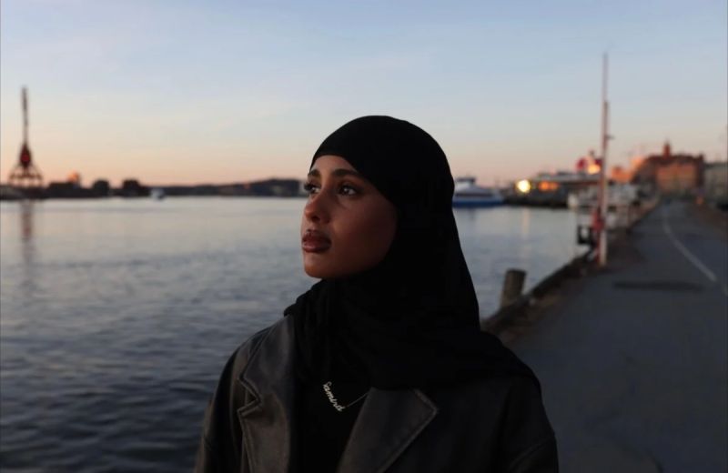 Porträtt i skymningsljus på Samira Hassan i slöja som står vid en kaj med stad och vatten i bakgrunden.