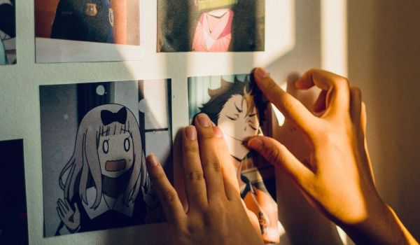 Två händer justerar utskrivna animebilder på en vägg i varmt solljus