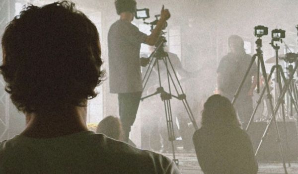 Kameraman ger tummen upp under en rökig videoinspelning av ett band, sett bakifrån publiken.