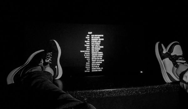 Svartvit bild på fötter som vilar mot en rad i en biosalong medan eftertexterna rullar på duken.