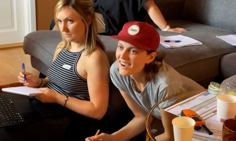 Två unga personer sitter på golvet och antecknar och lyssnar uppmärksamt under ett möte.