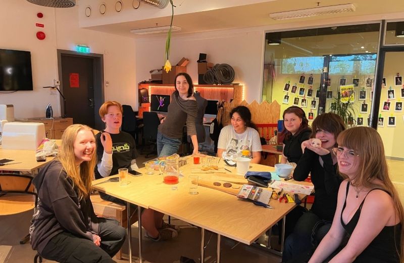 En bild på en grupp unga som sitter samlade runt ett bord och skapar.