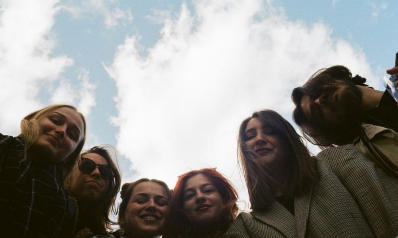 Sex ungdomar tittar ner i kameran underifrån mot en ljusblå himmel med vita moln.