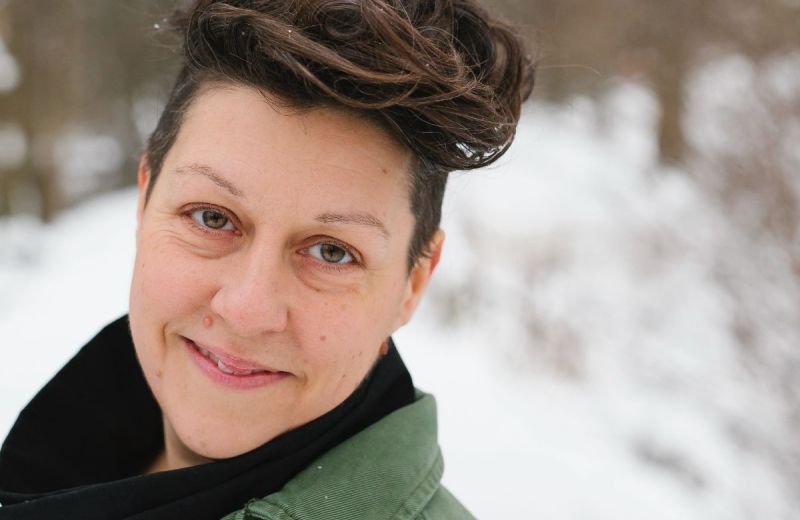 Ami-Ro Sköld ler mot kameran i en grön jacka med snötäckta träd i bakgrunden