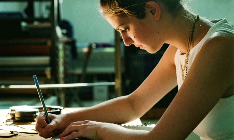 Närbild på en ung kreatör i profil som fokuserat antecknar i ett block under en skrivprocess.