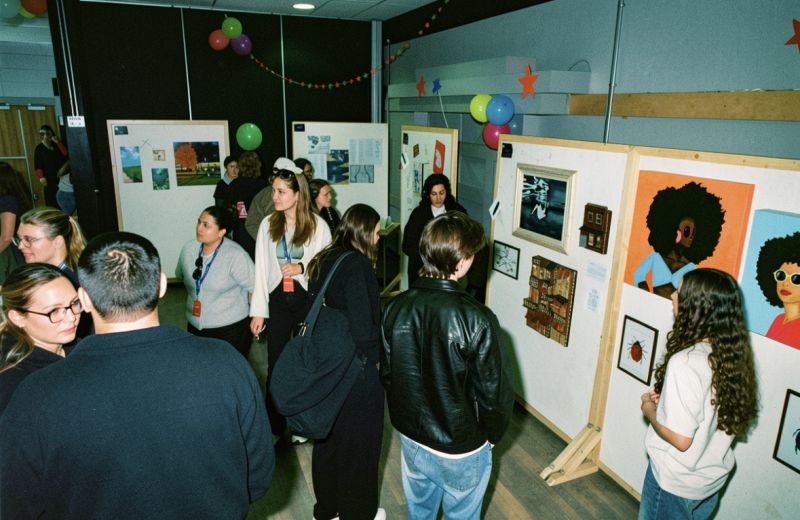 Besökare betraktar målningar och illustrationer under en konstutställning prydd med stjärnor och ballonger.