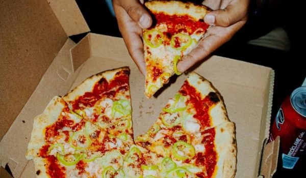 En hand lyfter en pizzaslice ur kartongen medan resten av pizzan ligger kvar