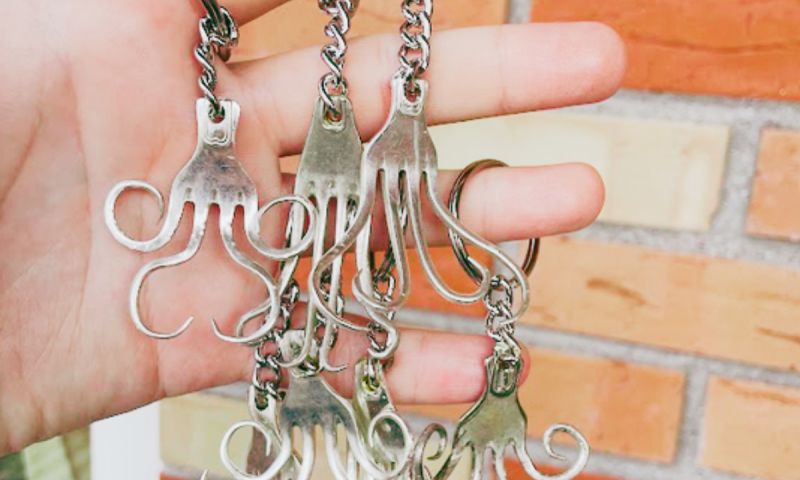 Närbild på handgjorda smycken och nyckelringar skapade av återbrukade silverbestick mot en tegelvägg.