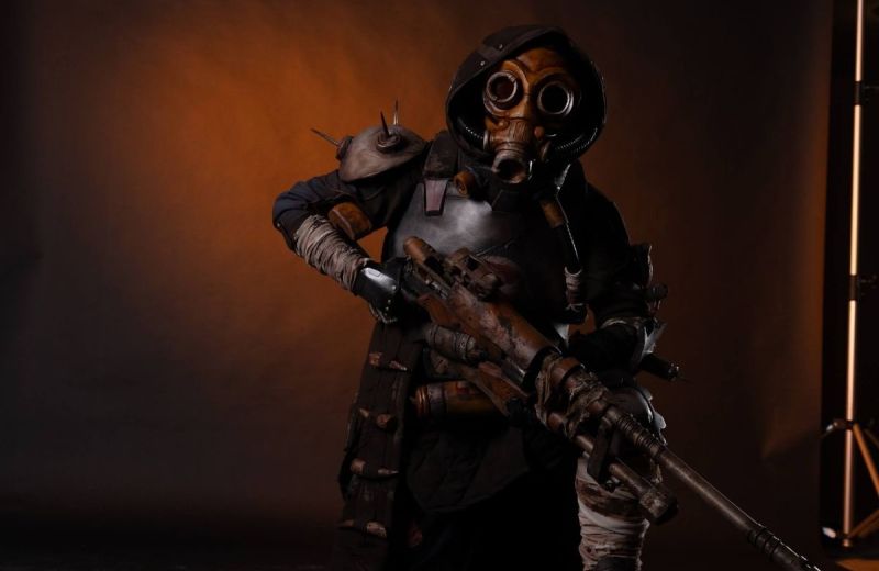 Detaljrik cosplay-dräkt i postapokalyptisk stil med gasmask och ett stort, patinerat gevär i mjuk studiobelysning.