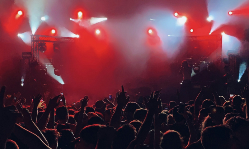 Konsertpublik sträcker händerna mot scenen under starka röda och vita scenljus