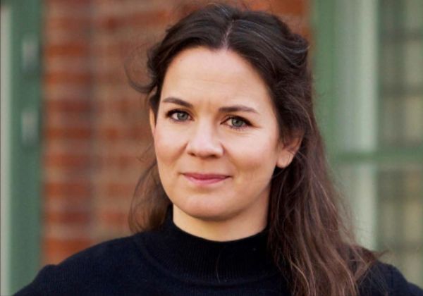 Ett porträtt av Astrid Ekermo som tittar lugnt in i kameran. Hon har långt mörkt hår och bär en svart polotröja. Bakgrunden består av en röd tegelvägg.