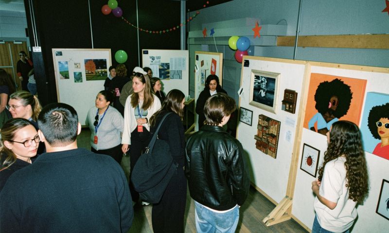 Besökare betraktar målningar och illustrationer under en konstutställning prydd med stjärnor och ballonger.
