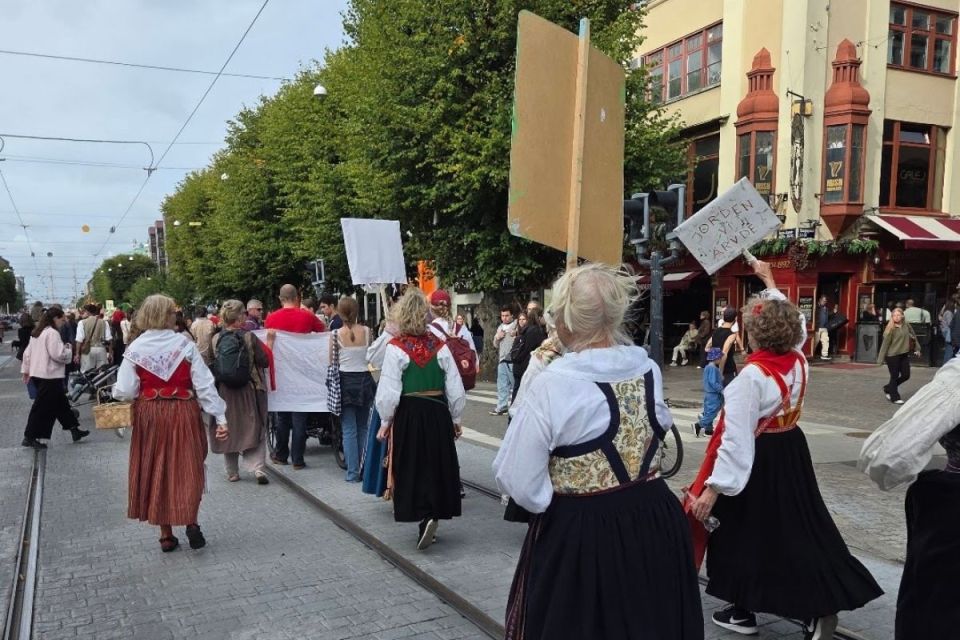 Människor i folkdräkter demonstrerar på en öppen gata med skyltar i händerna.