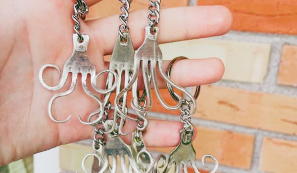 Närbild på handgjorda smycken och nyckelringar skapade av återbrukade silverbestick mot en tegelvägg.