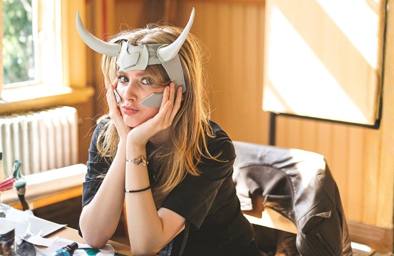 Person med hornförsedd hjälm vilar huvudet i händerna vid ett arbetsbord med pysselmaterial.