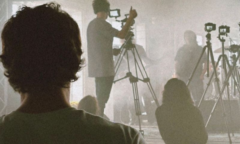 Kameraman ger tummen upp under en rökig videoinspelning av ett band, sett bakifrån publiken.