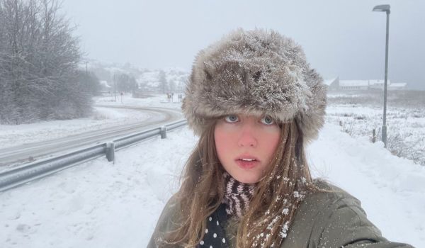 En selfie på poeten Alma Nyström Larsson iförd en fluffig mössa i snöig miljö, med en väg som går bredvid.