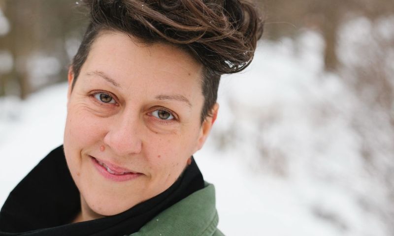 Ami-Ro Sköld ler mot kameran i en grön jacka med snötäckta träd i bakgrunden