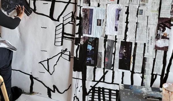 Person arbetar på ett stort blandteknik-konstverk med collage och svarta penseldrag.