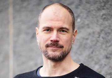 Erik Lundin i svart tröja blickar in i kameran mot en grå, suddig bakgrund.
