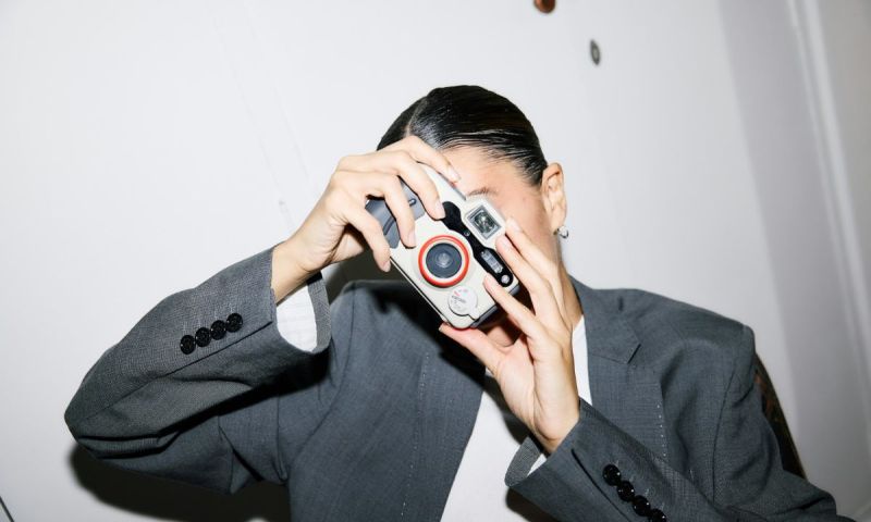 Person i grå kostym tar ett foto med en ljus kompaktkamera