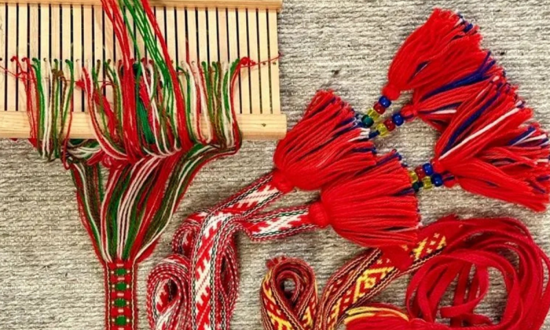 Färdiga och pågående vävda band med röda tofsar ligger bredvid en liten vävram