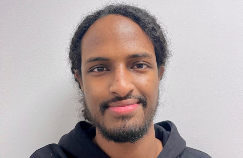 Närbild på Mohamed Yosef, framför en ljus vägg i mörk hoodie