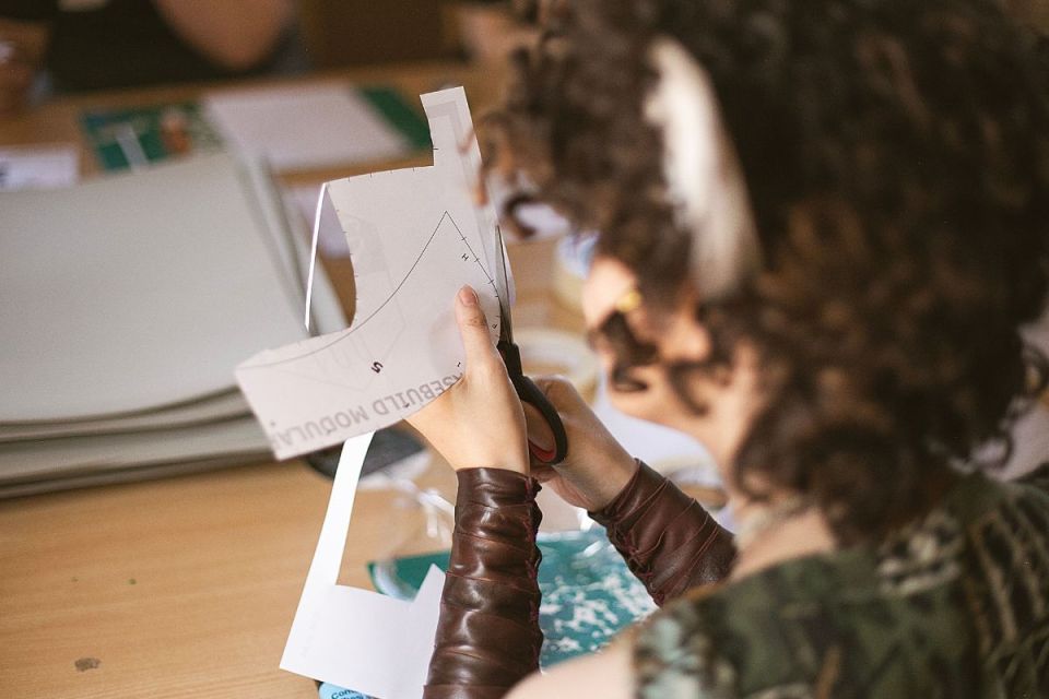 Närbild på en person som klipper ut en pappersmall med en sax vid ett arbetsbord.