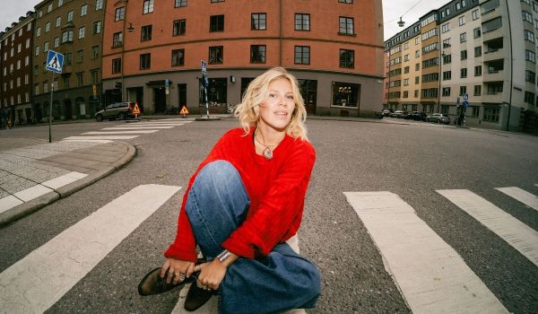 En ung kvinna sitter på ett övergångsställe och blickar in i kameran.