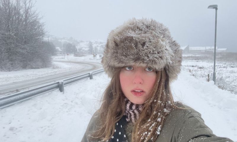 En selfie på poeten Alma Nyström Larsson iförd en fluffig mössa i snöig miljö, med en väg som går bredvid.
