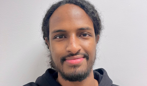 Närbild på Mohamed Yosef, framför en ljus vägg i mörk hoodie