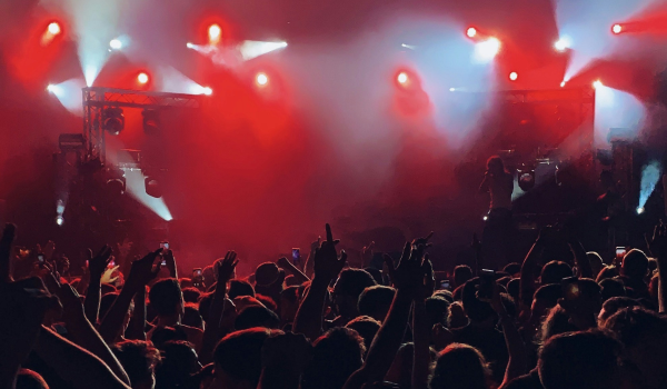 Konsertpublik sträcker händerna mot scenen under starka röda och vita scenljus