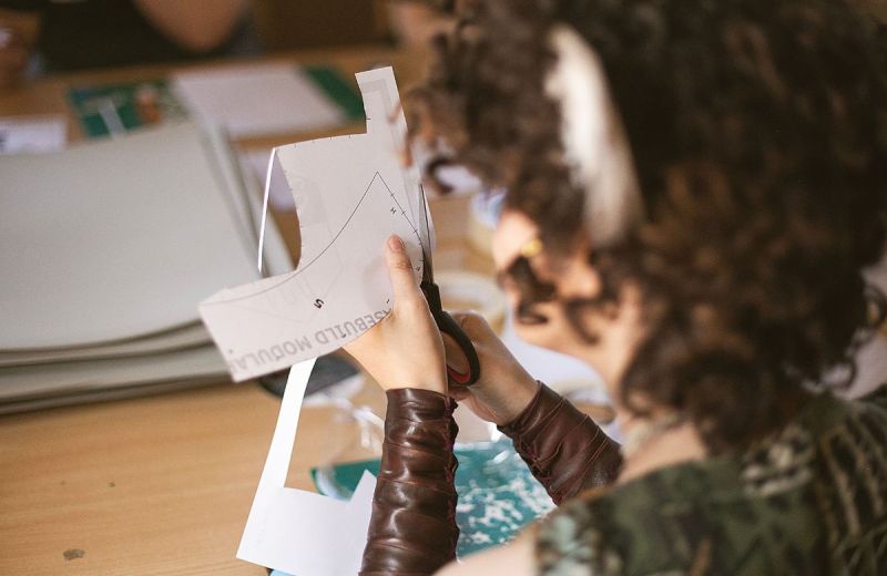 Närbild på en person som klipper ut en pappersmall med en sax vid ett arbetsbord.