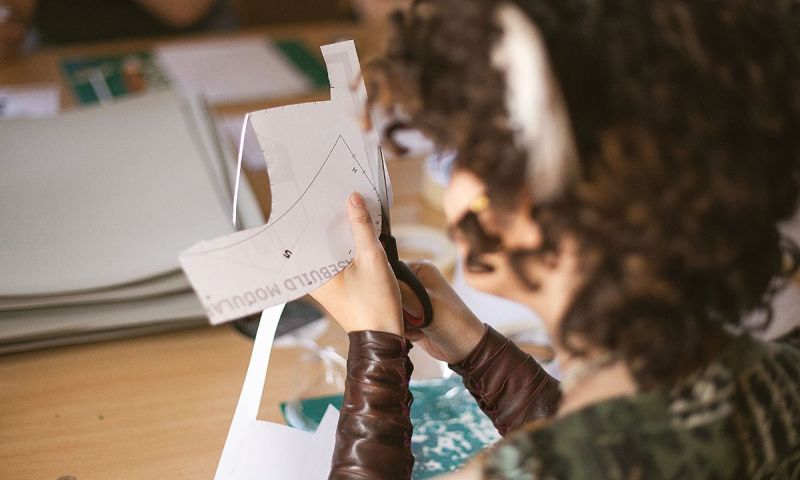 Närbild på en person som klipper ut en pappersmall med en sax vid ett arbetsbord.