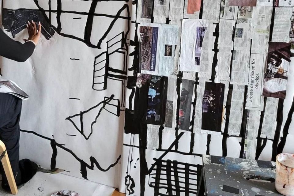 Person arbetar på ett stort blandteknik-konstverk med collage och svarta penseldrag.