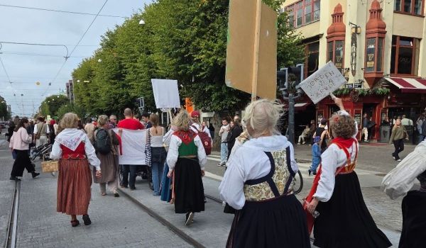 Människor i folkdräkter demonstrerar på en öppen gata med skyltar i händerna.