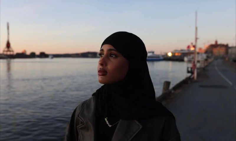 Porträtt i skymningsljus på Samira Hassan i slöja som står vid en kaj med stad och vatten i bakgrunden.