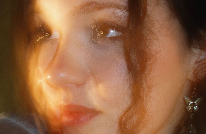 Närbild i varmt ljus på krönikören Lovisa Fhager. Hon har lockigt hår och ett glittrigt fjärilsörhänge.