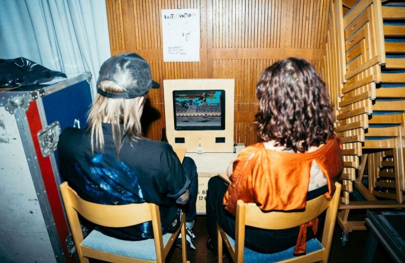 Två personer sitter och spelar ett retro-arkadspel på en hemmagjord träkonsol