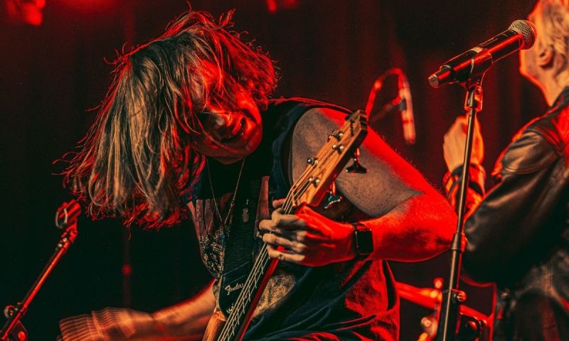 En basist spelar intensivt på en scen i starkt rött ljus.