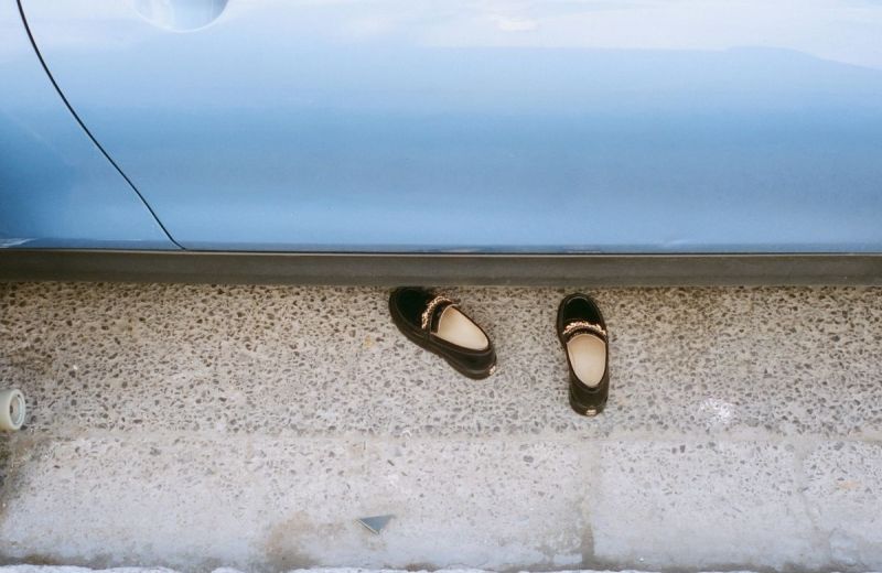 Ett par svarta skor med gulddetaljer på marken intill en ljusblå vägg